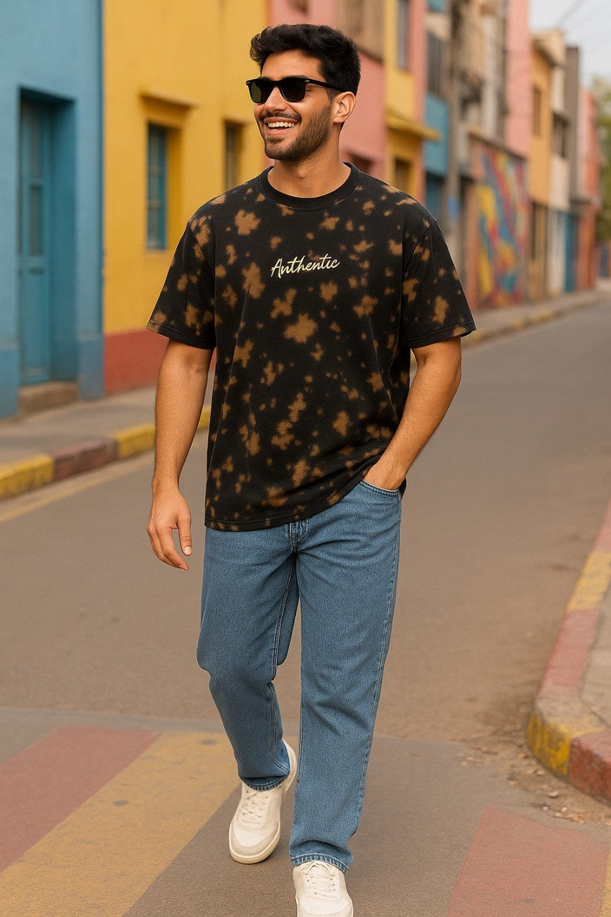 Man wearing a black tie-dye Embroidered 'Authentic' Unisex Oversized t-shirt  from The Edi Archive, and blue jeans walking on a colorful street.