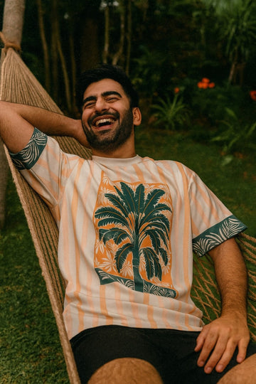 Man relaxing in a hammock wearing Azure Palms Unisex Oversized t-shirt from The Edi Archive, with a palm tree design.