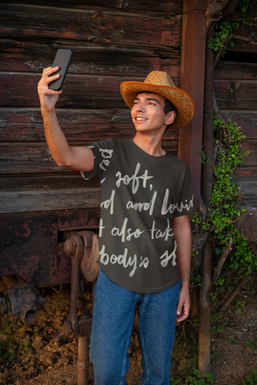 Person wearing a cowboy hat and graphic t-shirt Be Kind from The Edi Archive taking a selfie in front of a rustic wooden wall.