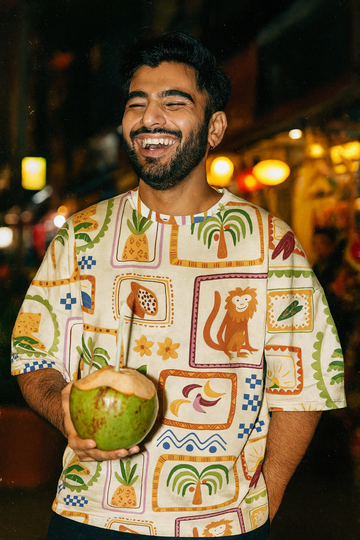 Man holding a coconut wearing a patterned shirt Flora and Fauna Unisex Oversized T-Shirt from The Edi Archive, with a blurred background