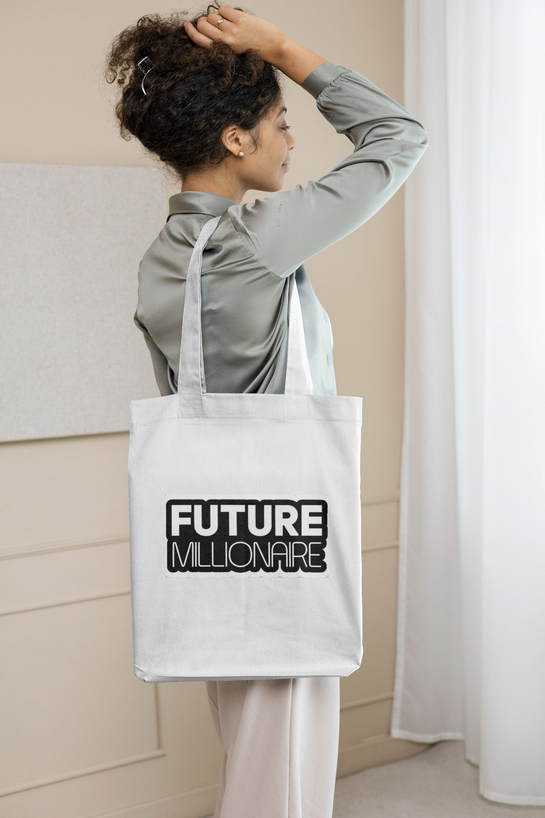 Person holding a tote bag with 'Future Millionaire' text by a waterfront.