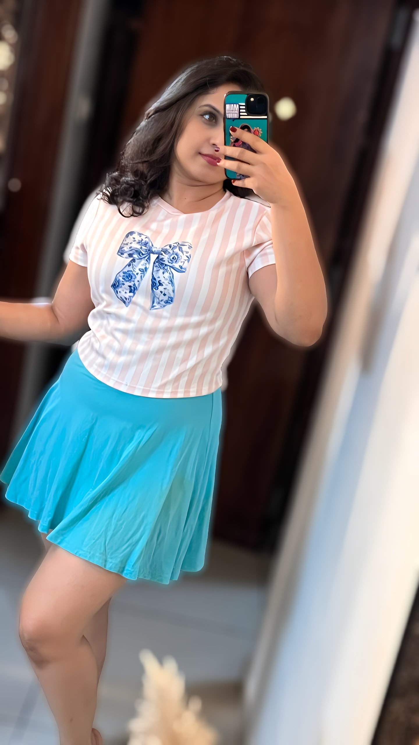 Woman wearing The Edi Archive’s Porcelain Bow crop top in pink and white stripes with a blue floral bow, styled with a pastel blue skirt from The Soft Launch Collection.