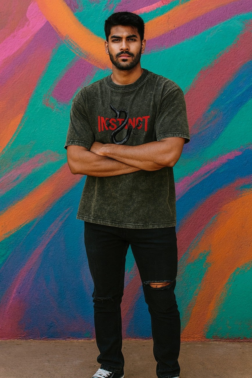 Man an Olive Grey, Instinct Unisex Oversized T-Shirt from The Edi Archive, against a colorful abstract wall.