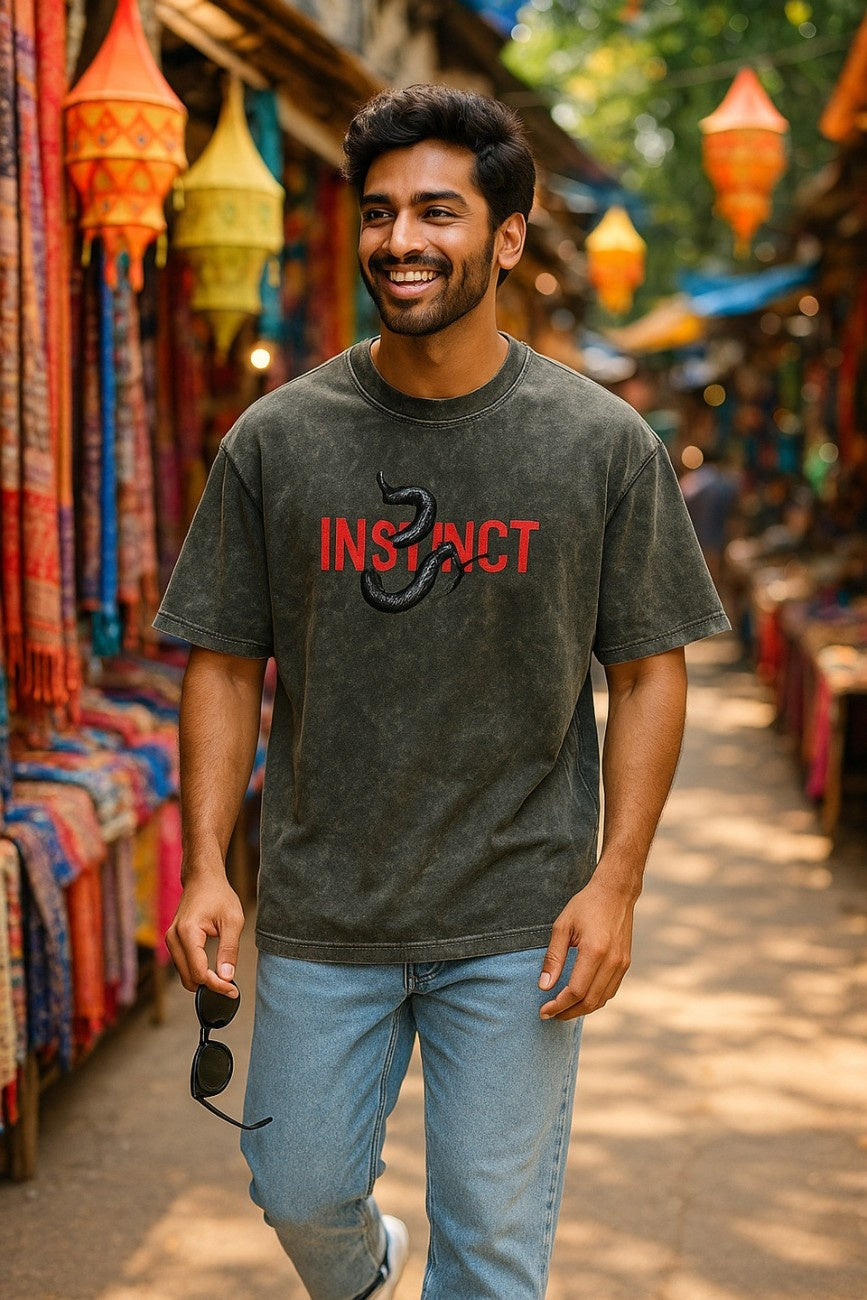 Man wearing an Olive Grey, Instinct Unisex Oversized T-Shirt from The Edi Archive, in a market setting