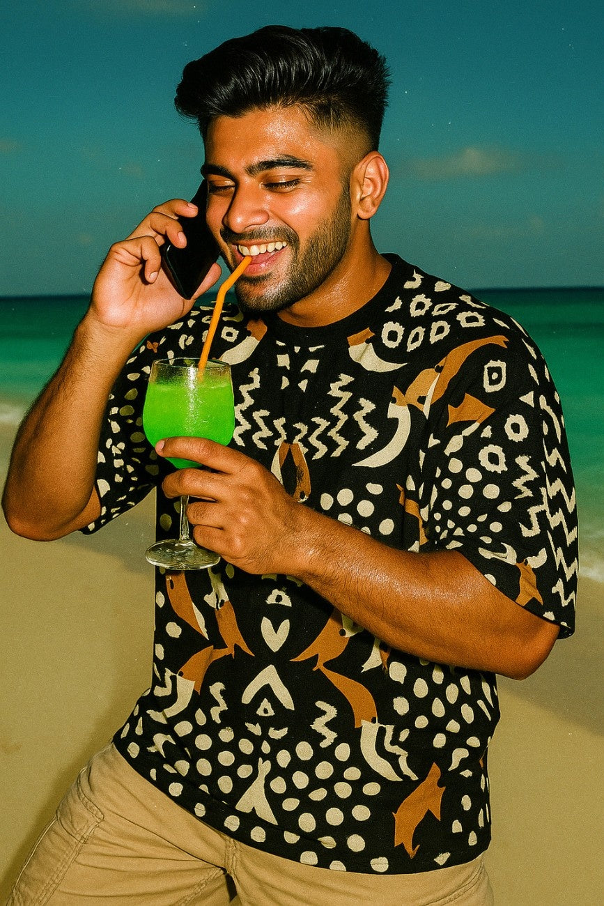 Man on a beach holding a colorful drink wearing Pelican Breeze Unisex Oversized T-Shirt from The Edi Archive, and talking on a phone