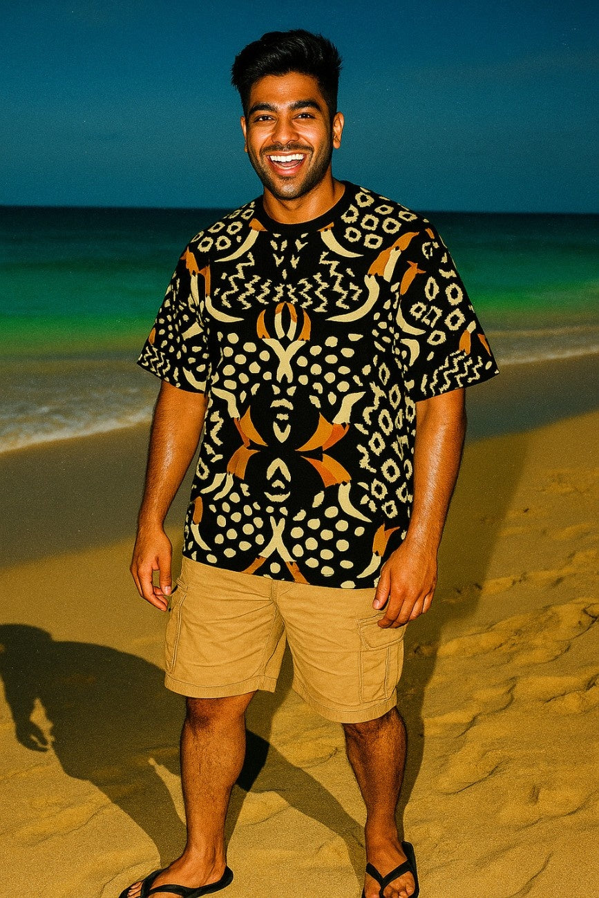 Man wearing a Pelican Breeze Unisex Oversized T-Shirt from The Edi Archive, and beige shorts standing on a beach with ocean in the background