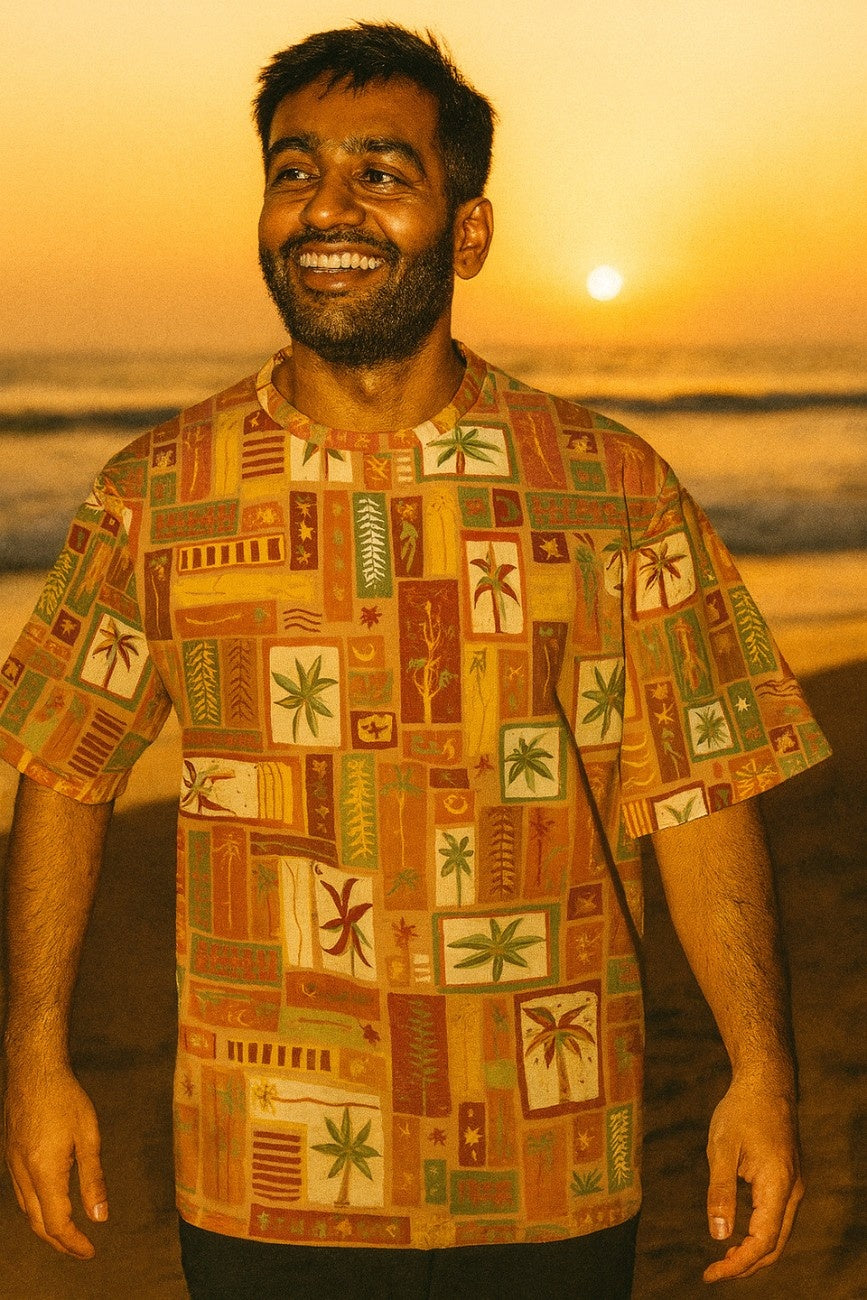 Man wearing a patterned Summer Dreams Unisex Oversized T-Shirt from The Edi Archive, on a beach at sunset