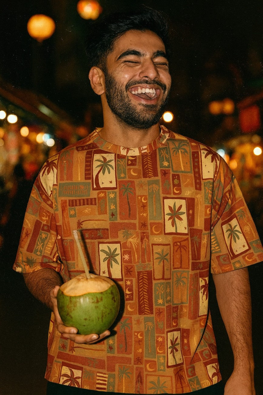 Man wearing a patterned Summer Dreams Unisex Oversized T-Shirt from The Edi Archive, on a beach at sunset