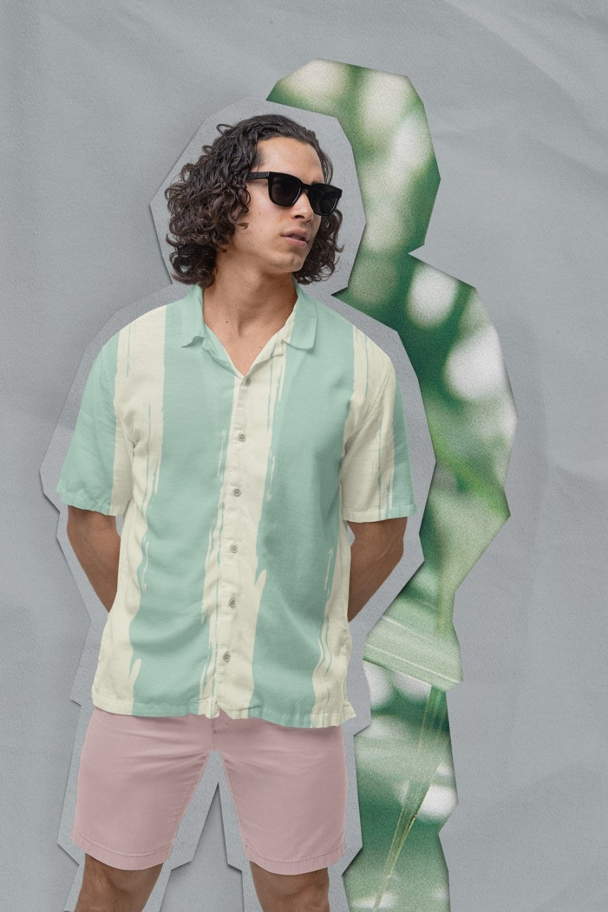 Man wearing Teal Away Men's Hawaiian Shirt from the Tropical Drops from The Edi Archive, and pink shorts against a gray background.