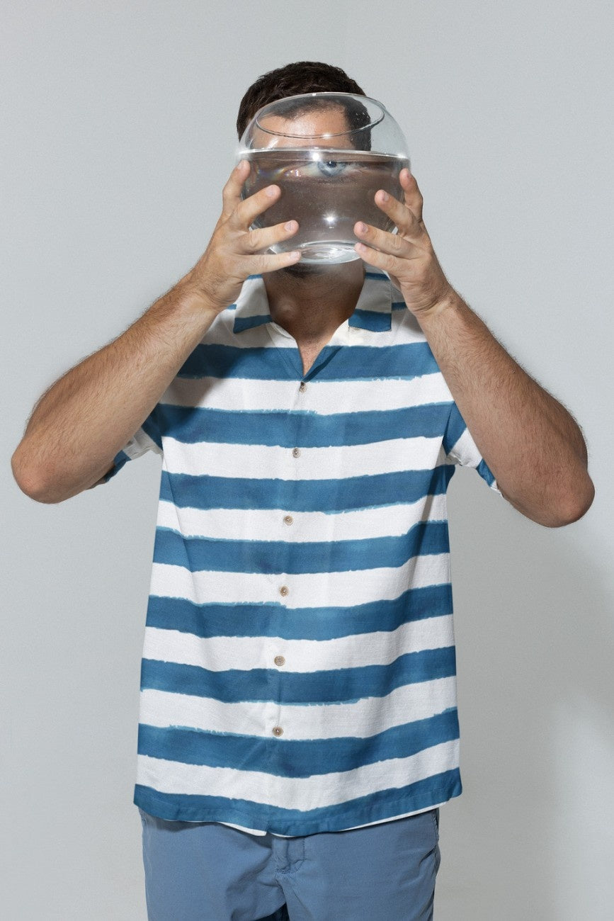 Person wearing a 'Stripe the Turquoise Men's Hawaiian Shirt' from Tropical Drops Collection from The Edi Archive holding a fishbowl.