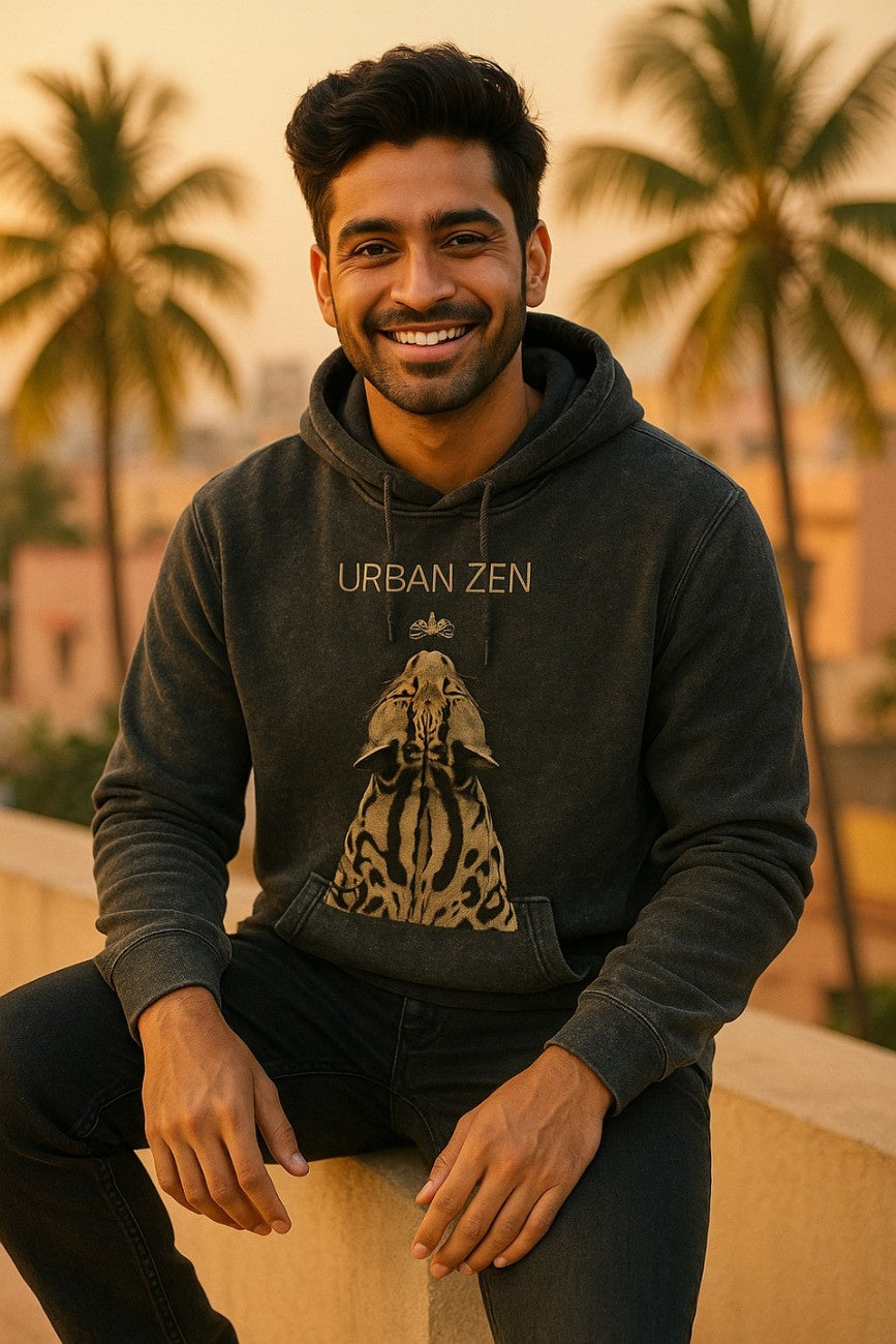 Man wearing a stone-washed black hoodie with 'Urban Zen' design from The Edi Archive, sitting outdoors with palm trees in the background