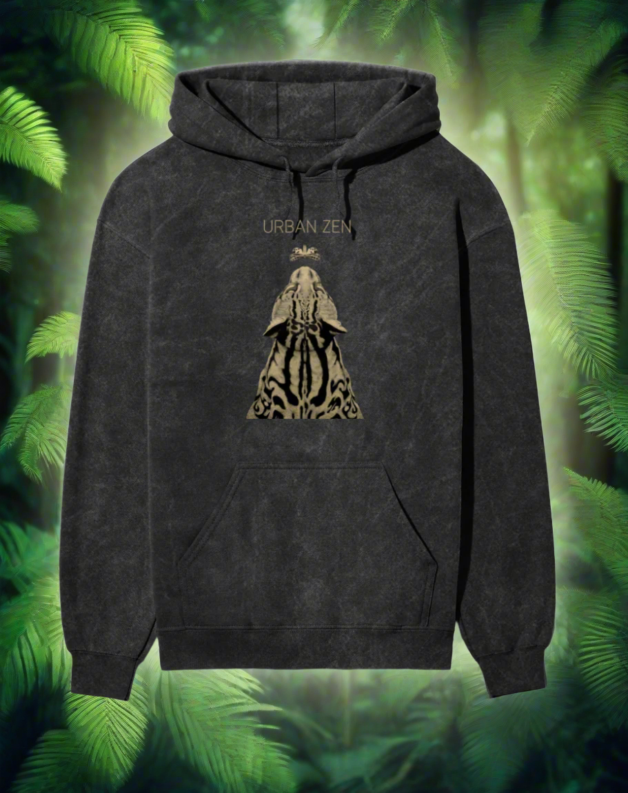 Man wearing a stone-washed black hoodie with 'Urban Zen' design from The Edi Archive, sitting outdoors with palm trees in the background
