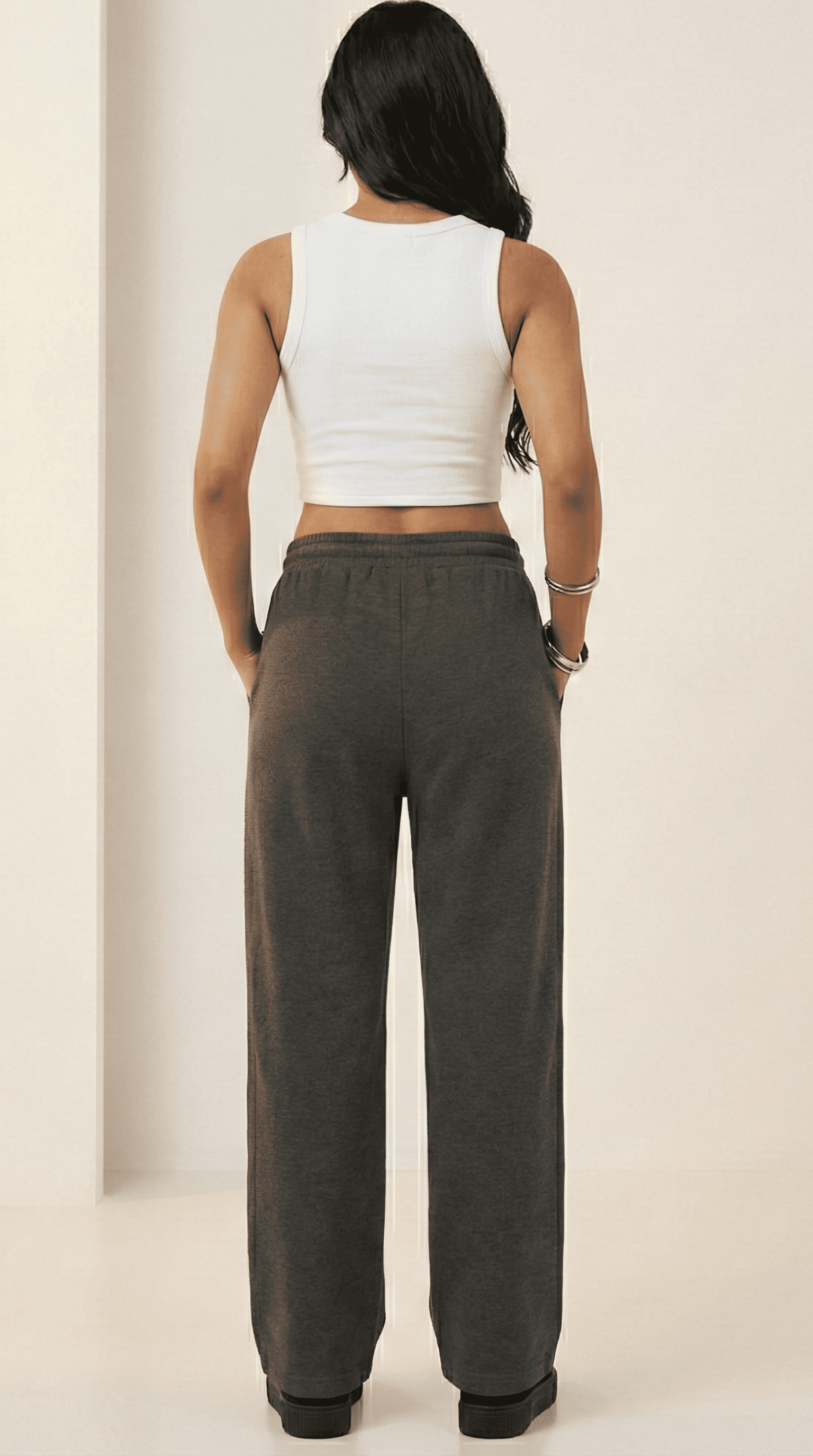 Woman wearing a white tank top and charcoal comfy chaos unisex sweatpants from The Edi Archive, back view.