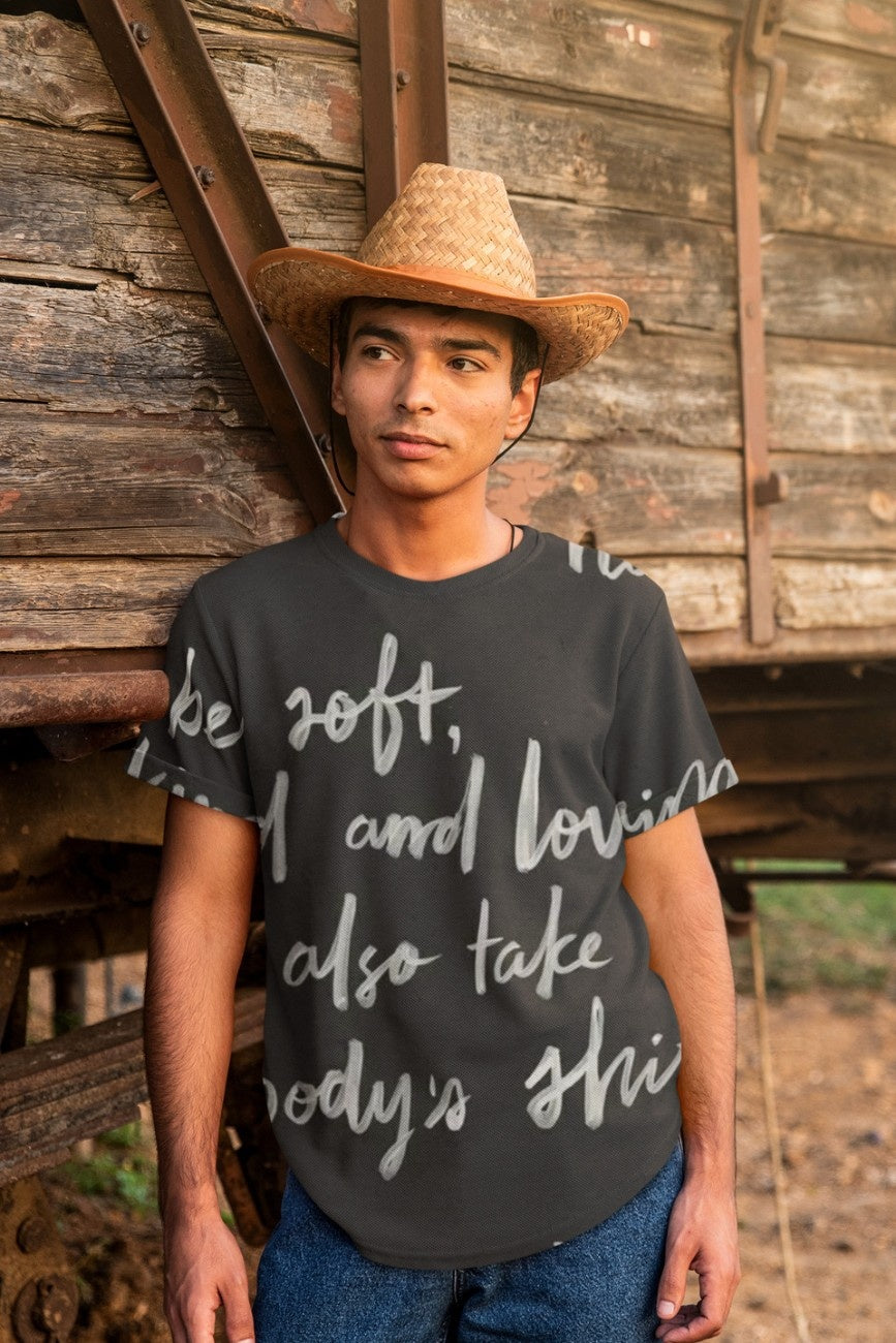 Person wearing a black oversized t-shirt Be Kind from The Edi Archive and a straw hat standing in front of a wooden wall.