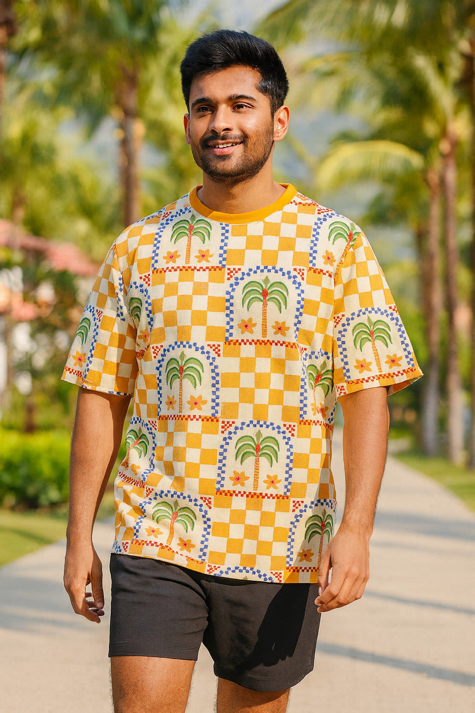 Man wearing a colorful patterned Desert Palm Unisex Oversized T-Shirt from The Edi Archive, with palm trees outdoors
