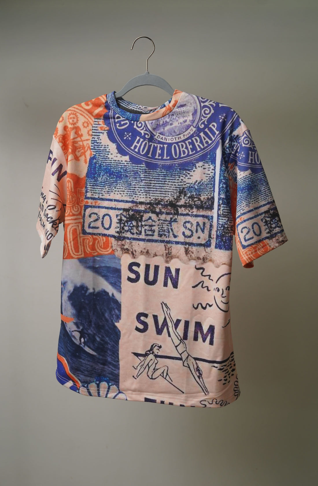 Man wearing a colorful patterned oversized t-shirt, Sun Swim Sea from The Edi Archive, standing in front of a graffiti wall.