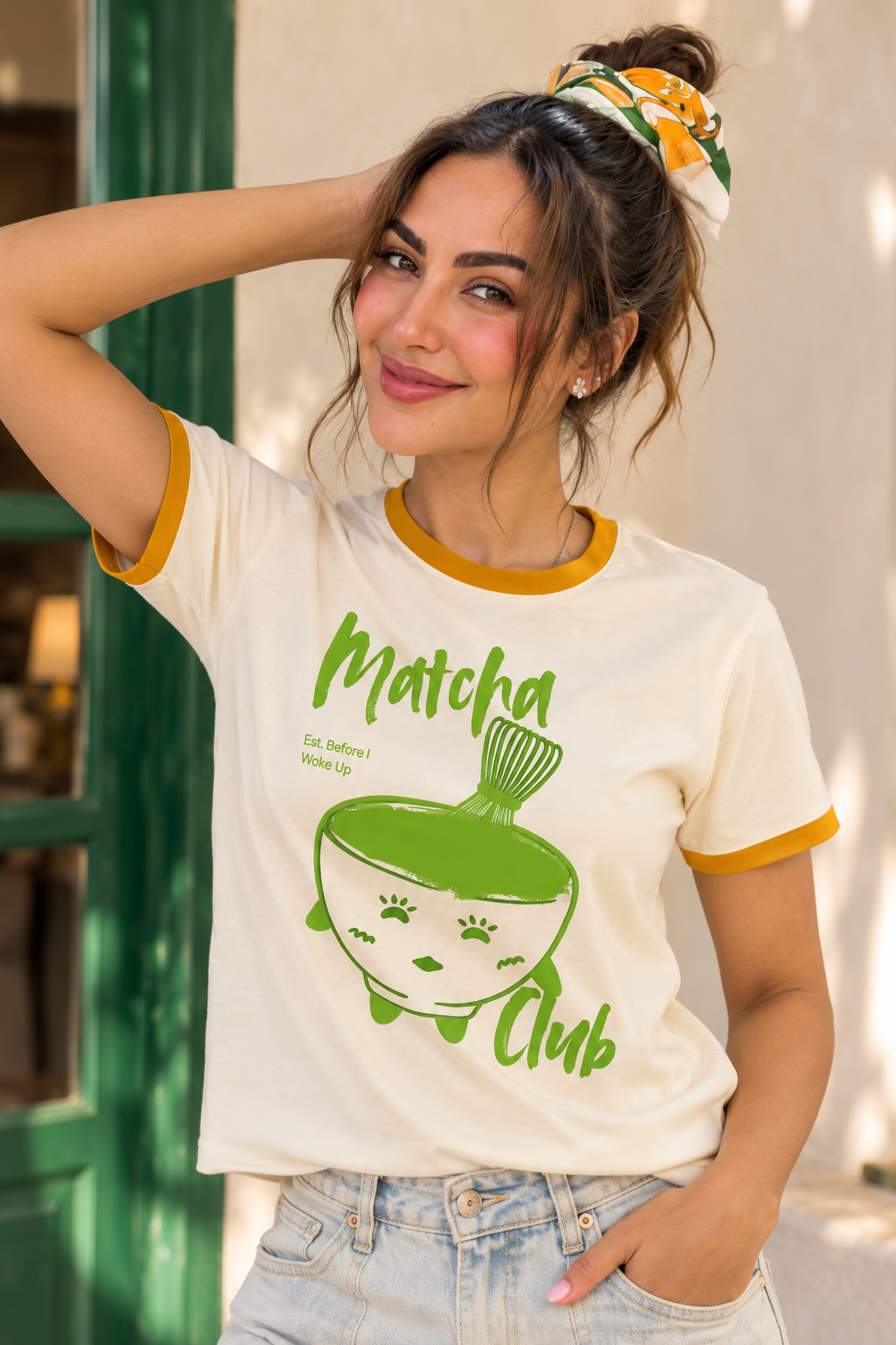 Close-up of a woman wearing the cream Matcha Club graphic ringer T-shirt with mustard contrast trim, showing the green kawaii matcha design on the front.
