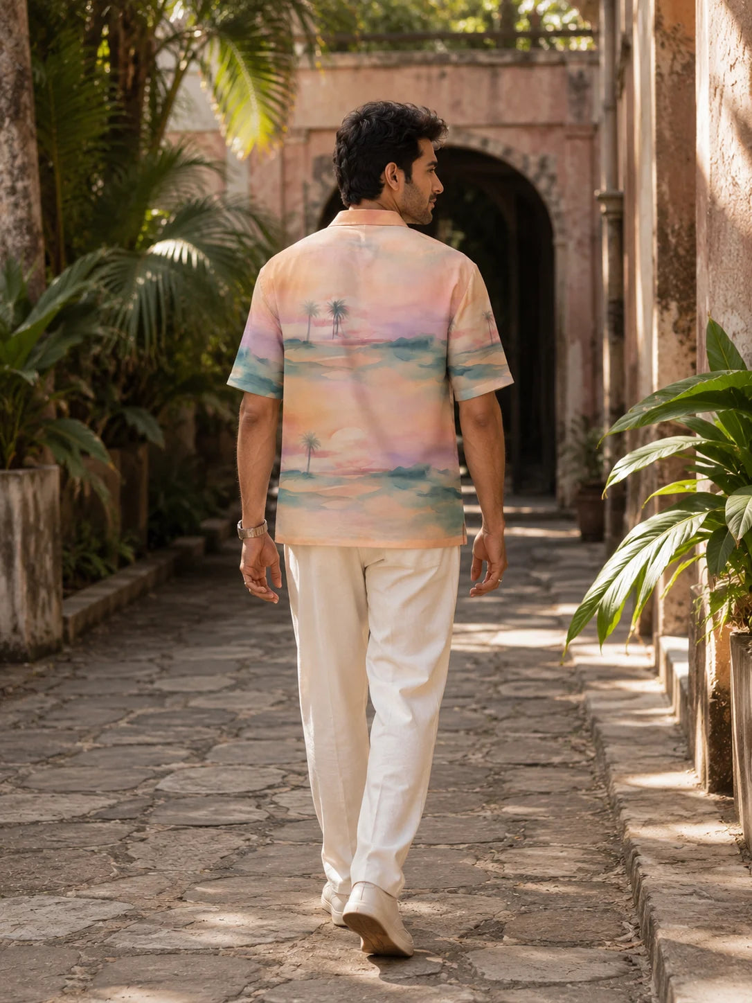  Back view of a man walking in a tropical sunset print Hawaiian shirt showing the full all over palm and ocean artwork, Mirage Hawaiian Shirt, Tropical Drop, The Edi Archive