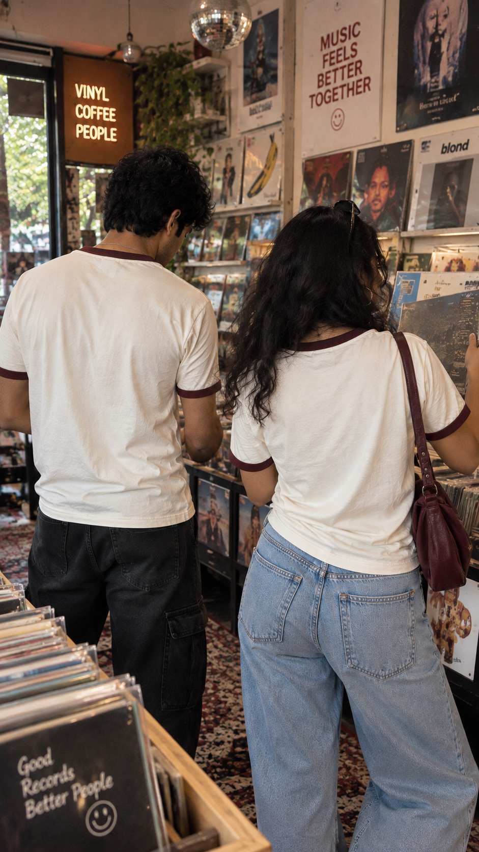 Back view of the Overdressed Ringer T-Shirt by The Edi Archive showing the cream cotton fabric with burgundy ribbed neckline and sleeve trims, worn at a vinyl record store
