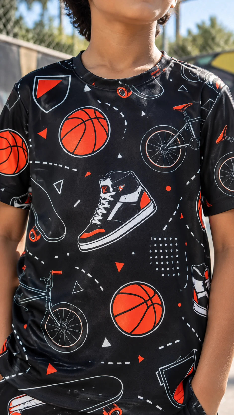 The Edi Archive Skate Sneakers kids T-shirt close-up showing basketball, skateboard, bicycle and high-top sneaker graphics on a black base